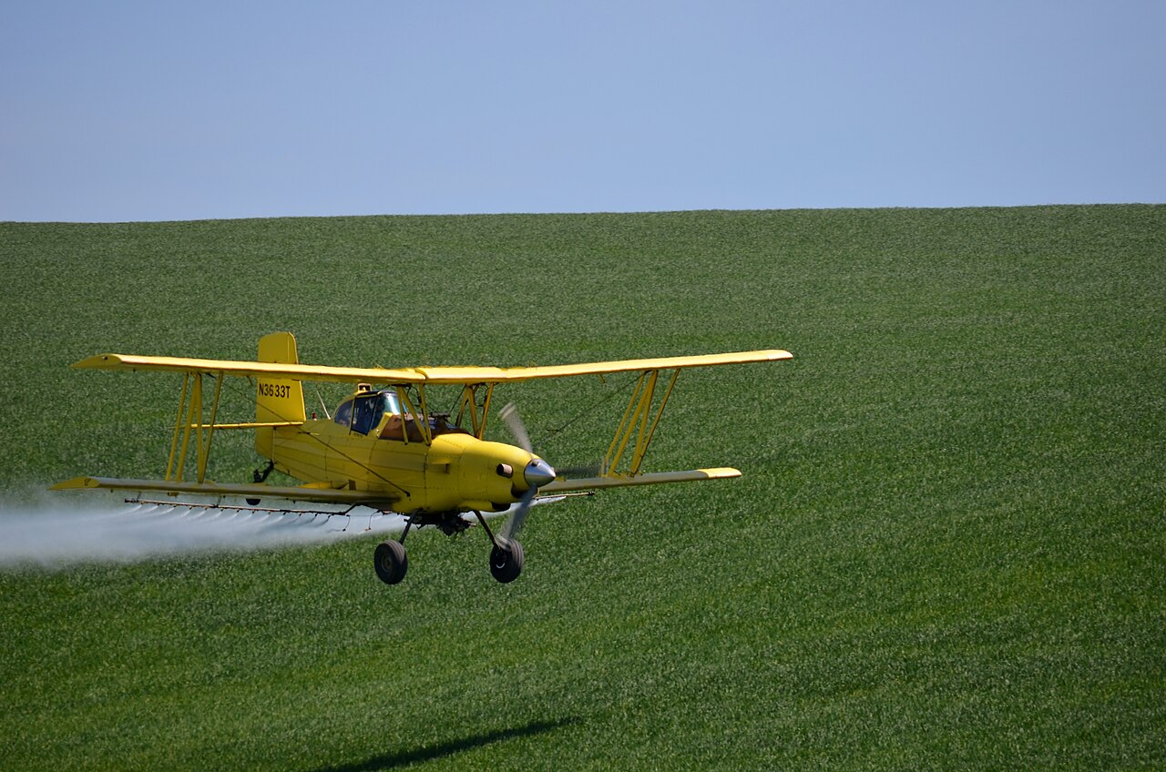 yellow crop duster spraying field